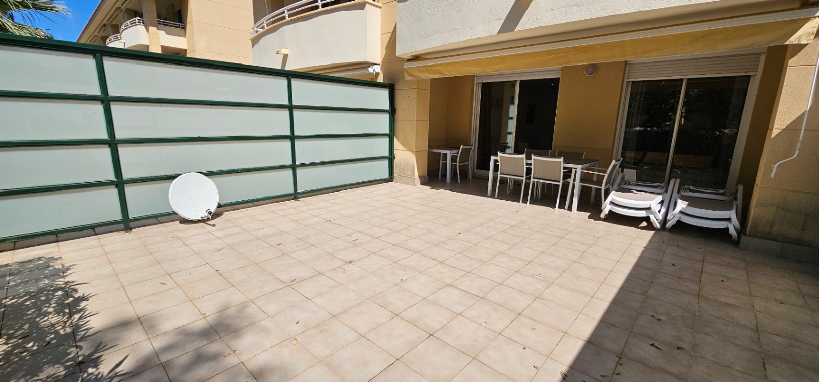 Terraza privada de planta baja con suelo cerámico, zona de comedor exterior bajo toldo retráctil y paneles de privacidad de cristal traslúcido.