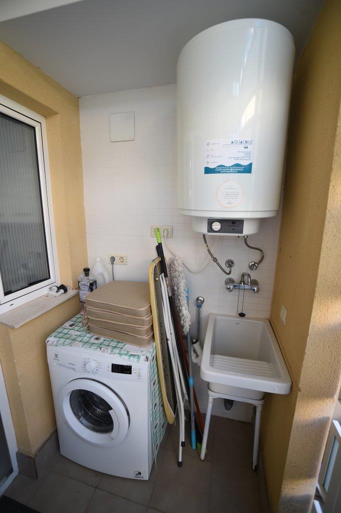 Zona de lavadero funcional equipada con lavadora, termo eléctrico de gran capacidad, pila de lavar y espacio para artículos de limpieza.