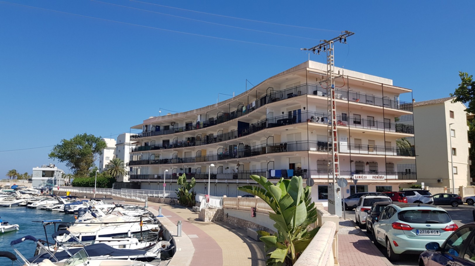 Edificio residencial de diseño curvo frente a la marina, con amplias terrazas perimetrales y vistas directas a los amarres de barcos en Jávea.