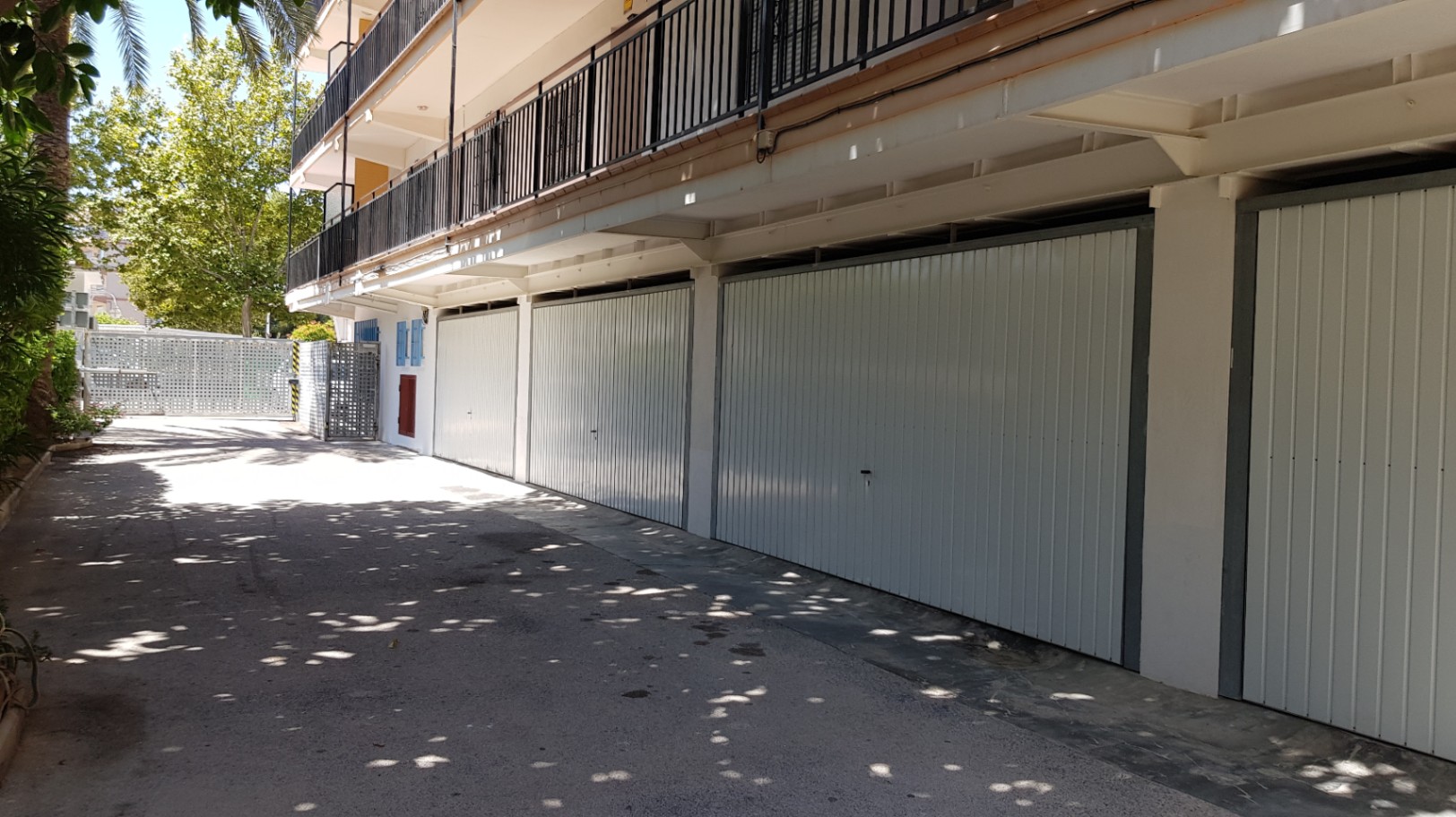 Garajes privados individuales con puertas metálicas blancas, situados en la planta baja del edificio con acceso directo desde el recinto pavimentado y sombreado.