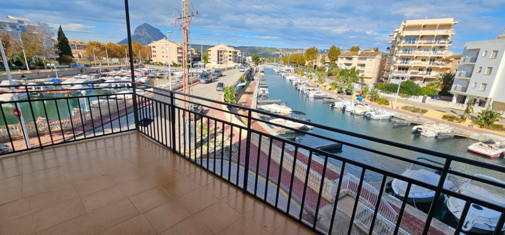Terraza con suelo cerámico y barandilla metálica negra que ofrece vistas directas al canal de la marina y al emblemático monte Montgó al fondo.
