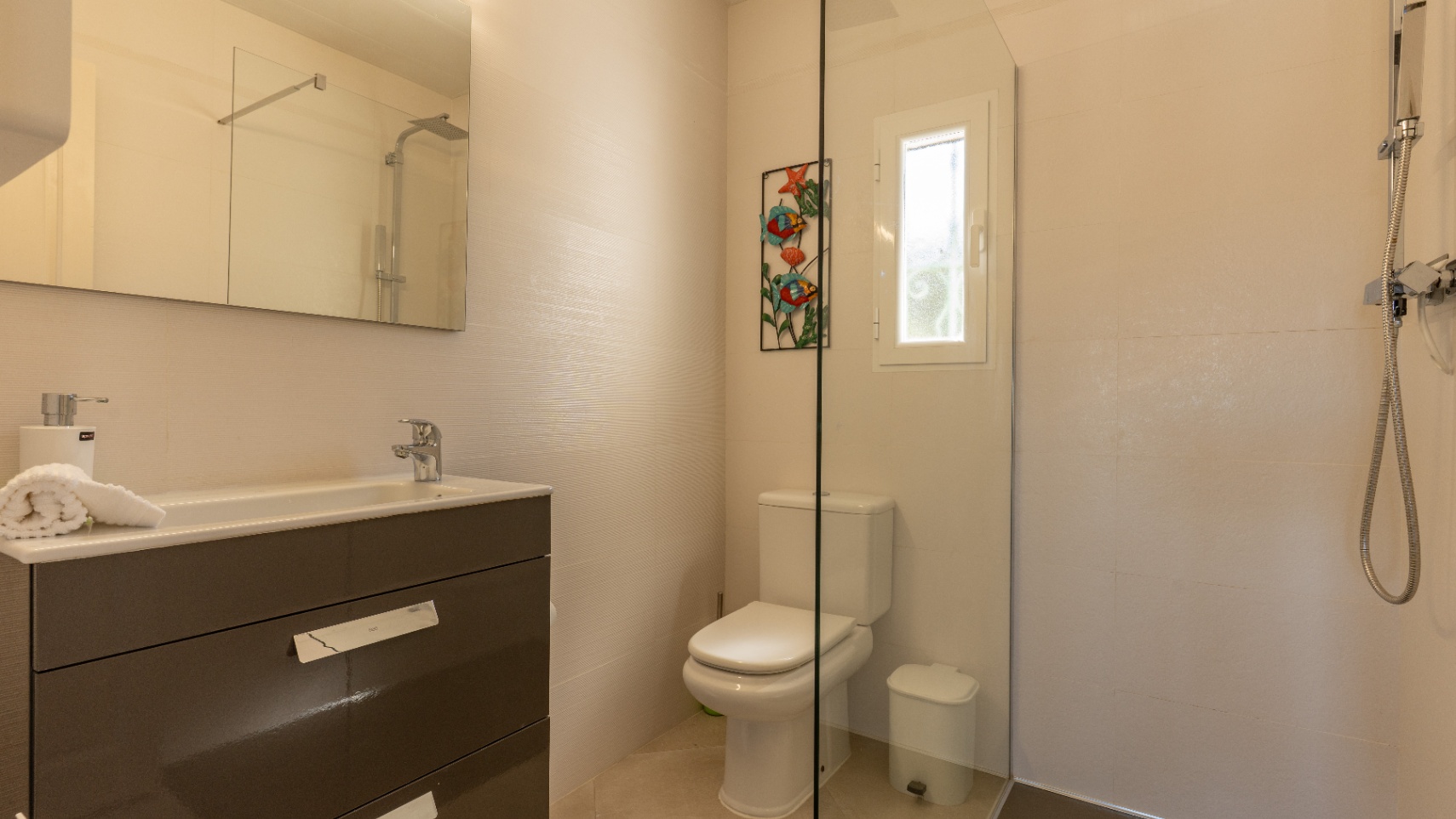 Baño moderno con mueble de lavabo en gris oscuro, espejo de gran formato y ducha con mampara de cristal fija y grifería cromada.