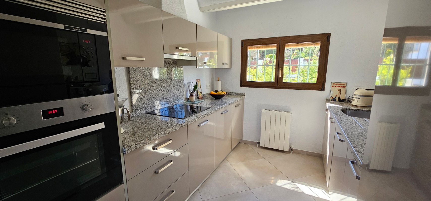 Cocina independiente con armarios de alto brillo, encimeras de granito y electrodomésticos integrados. La ventana de madera aporta luz natural y vistas al jardín.