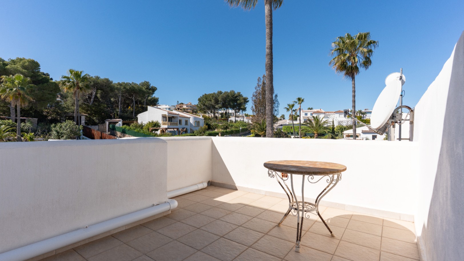 Terraza superior con suelos cerámicos y mesa de forja, equipada con antena parabólica y vistas despejadas al entorno arbolado de Pinosol.