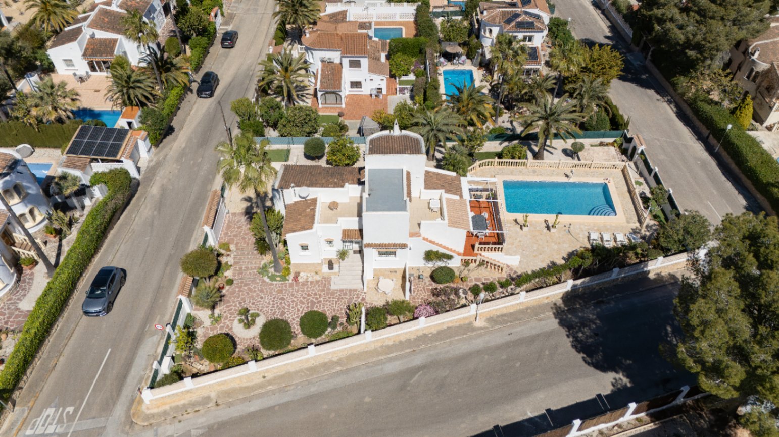 Vista aérea de la parcela en esquina con chalet de estilo mediterráneo, piscina rectangular, terrazas soleadas y jardín cuidado en la zona de Pinosol, Jávea.