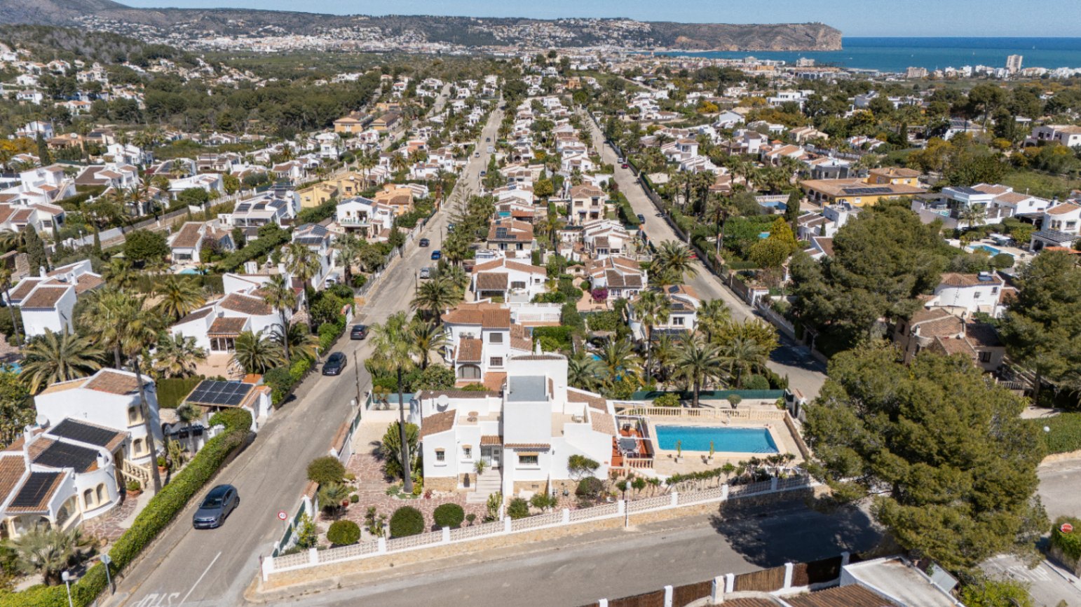 Vista aérea de la propiedad en Pinosol, destacando su fachada blanca, piscina privada y la cercanía al mar Mediterráneo en el horizonte de Jávea.