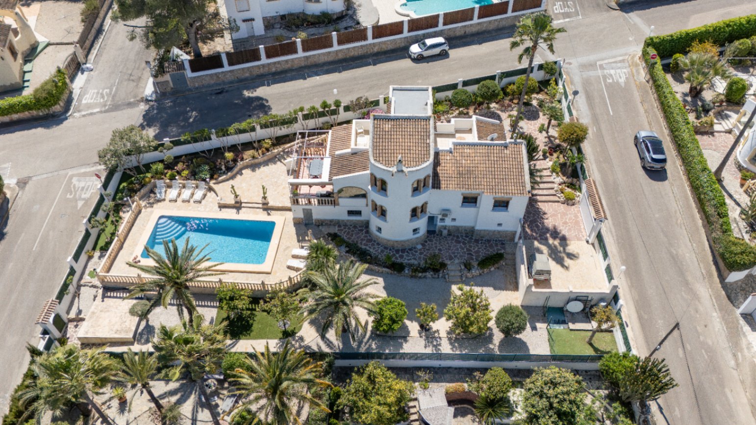 Vista aérea de la villa en Pinosol, Jávea, destacando su piscina privada rodeada de palmeras, terrazas de piedra y una arquitectura mediterránea con torre circular.