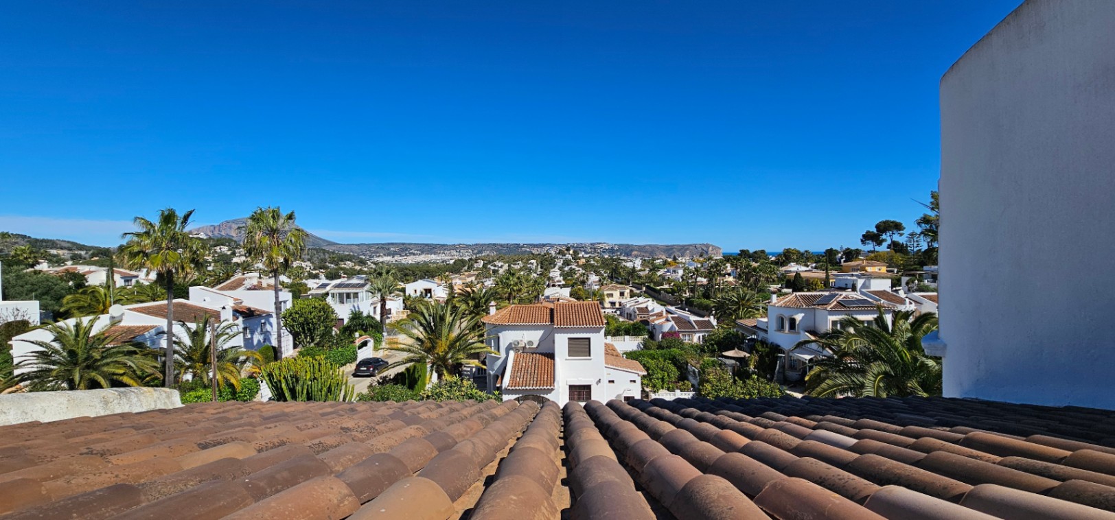Vista panorámica desde la azotea con tejas tradicionales, mostrando el paisaje residencial de Jávea, palmeras y el perfil del Montgó bajo un cielo despejado.