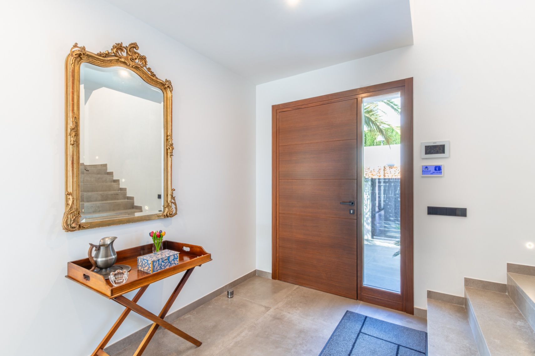 El vestíbulo de entrada presenta una gran puerta de madera con panel lateral acristalado, un espejo de marco dorado ornamentado y suelos de gres porcelánico.