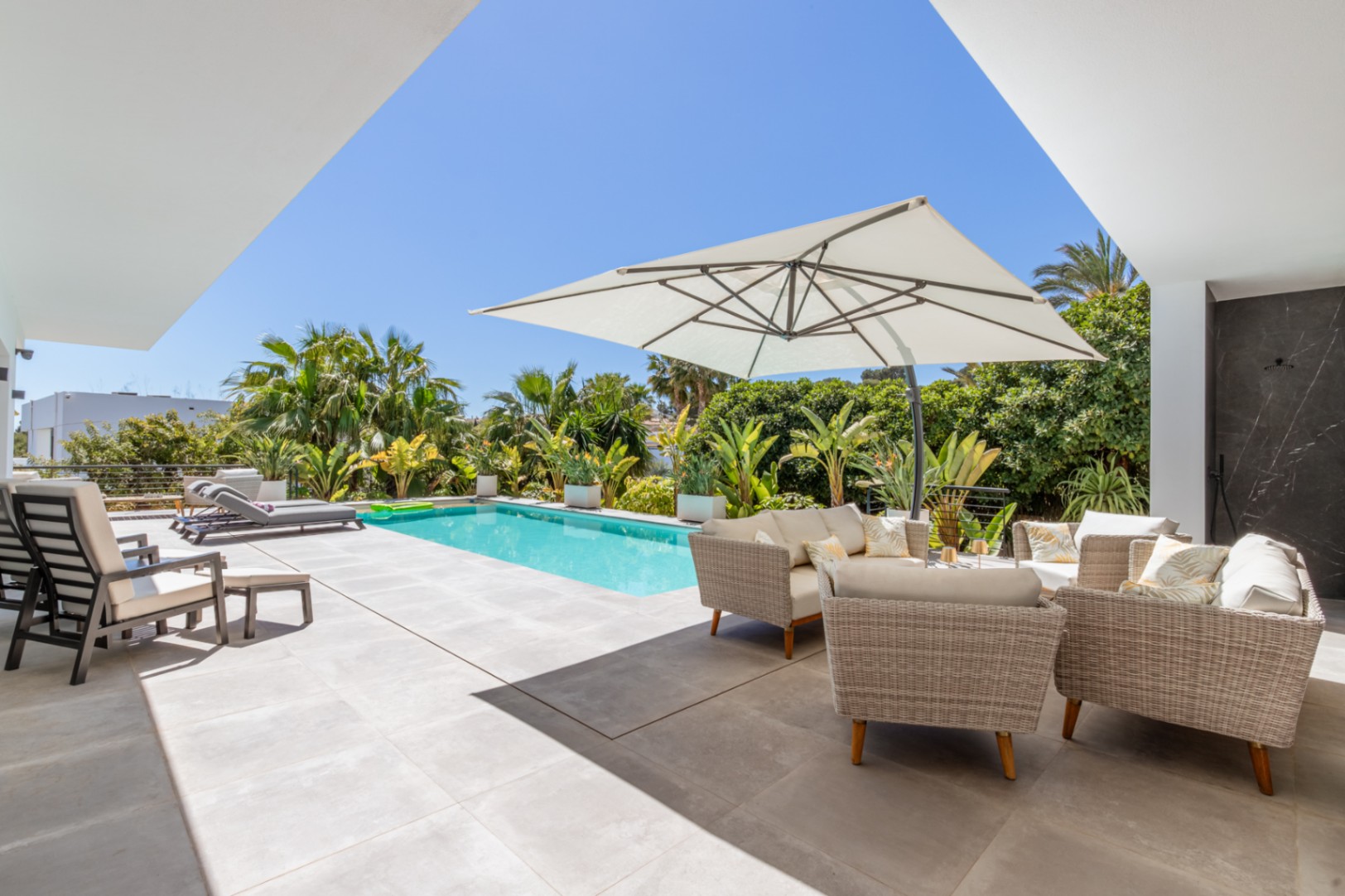 Terraza exterior con piscina rectangular, zona de estar con sofás de mimbre bajo sombrilla y vegetación mediterránea madura que aporta privacidad.