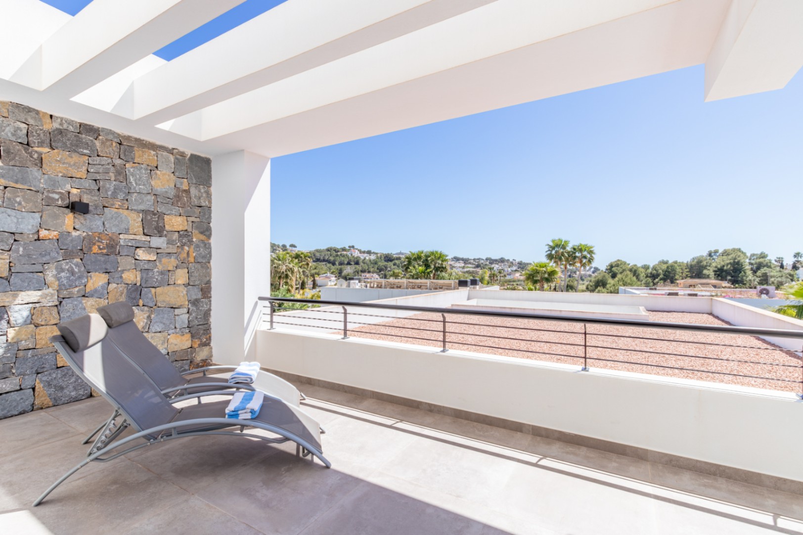 Terraza privada en la planta superior con pérgola blanca, pared de piedra natural y vistas despejadas hacia el paisaje de Moraira.