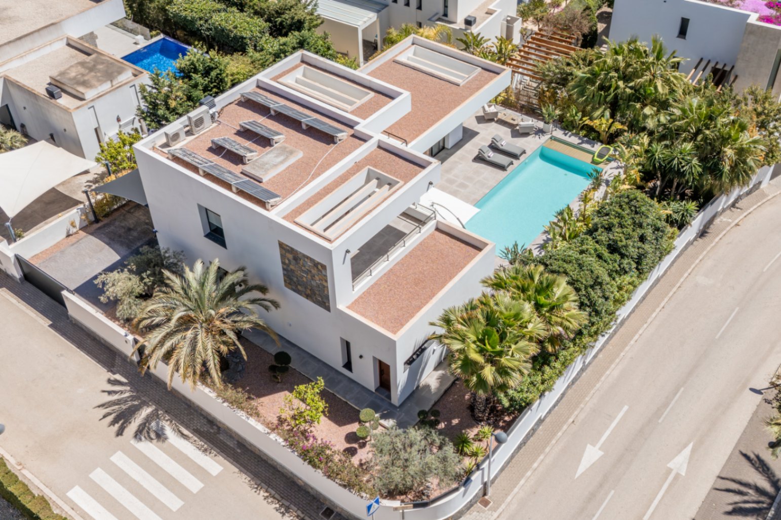 Vista aérea de la villa moderna con paneles solares, piscina privada y jardín mediterráneo perimetral que garantiza privacidad en una parcela de esquina.