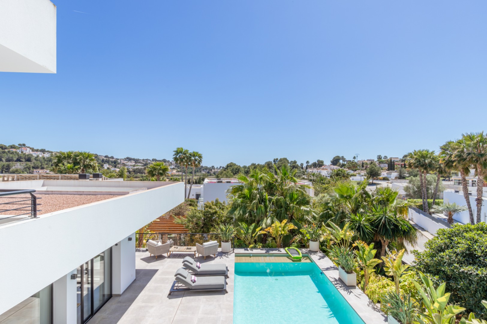 Vista elevada de la zona exterior con piscina rectangular, terraza de gres porcelánico y jardín mediterráneo maduro con palmeras que garantizan privacidad.