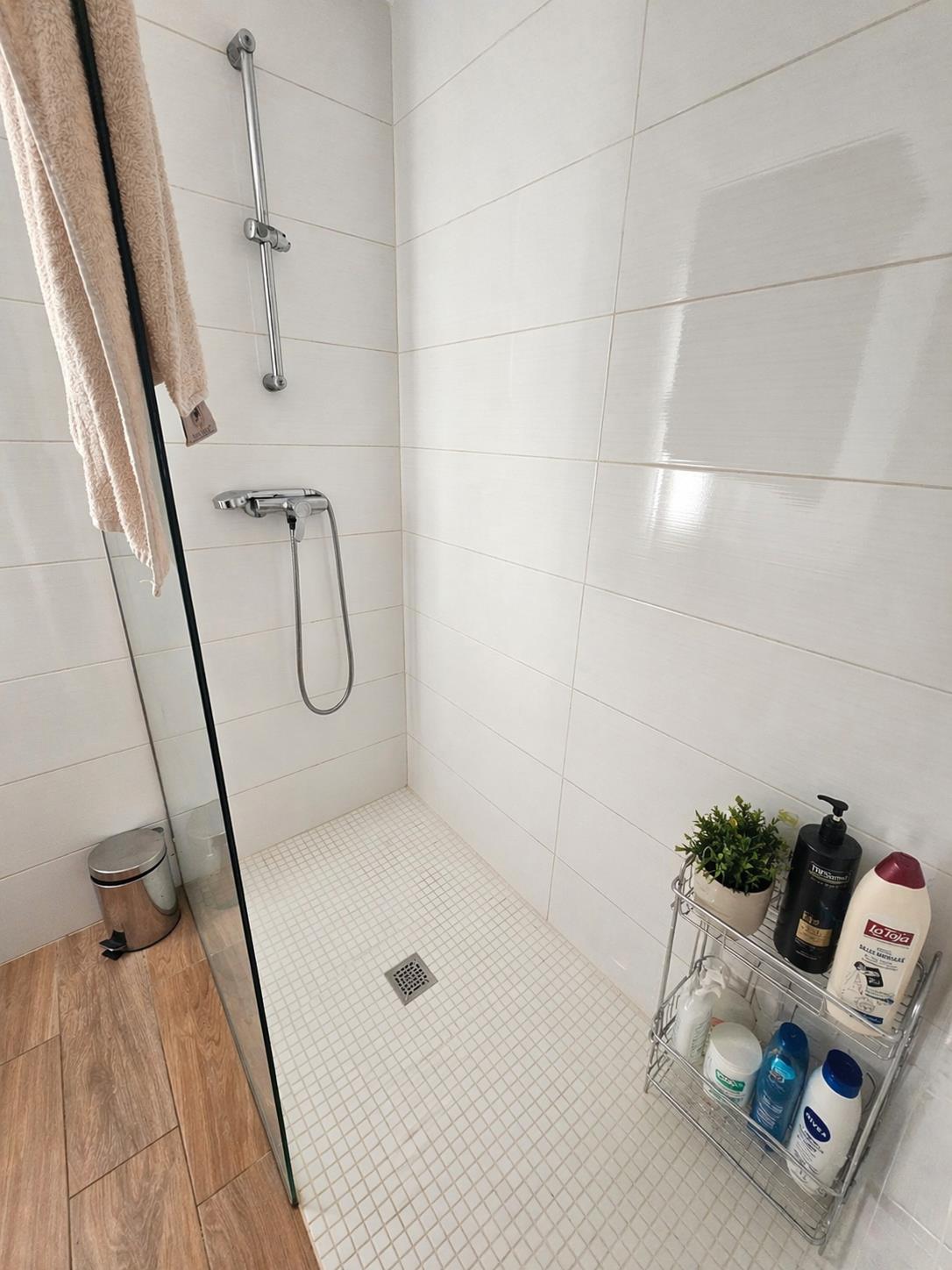 Ducha de estilo italiano con suelo de mosaico blanco, mampara de cristal y paredes revestidas con azulejos horizontales en tonos claros.