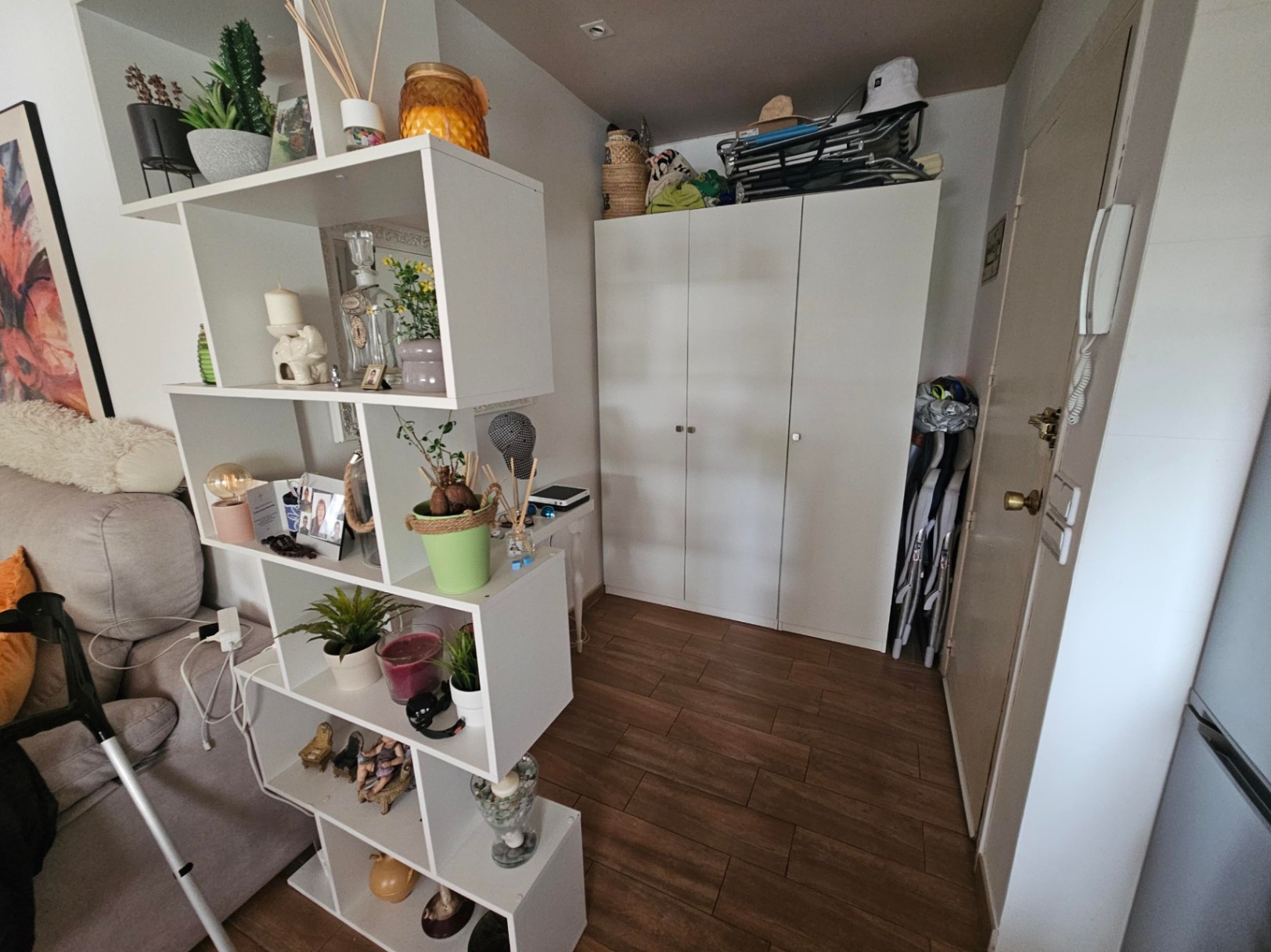 Hall de entrada con suelos de gres efecto madera, armario blanco de tres puertas y estantería modular decorativa que actúa como separador de ambientes.