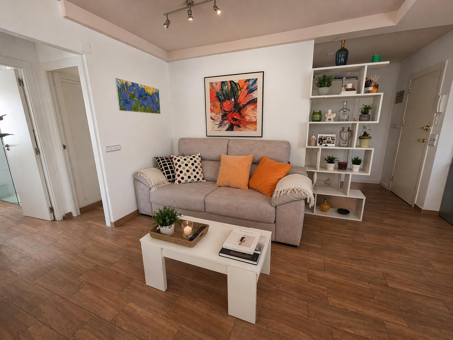 Salón acogedor con suelos de gres efecto madera, sofá tapizado en gris y estantería de diseño geométrico. La estancia destaca por su decoración moderna y funcional.