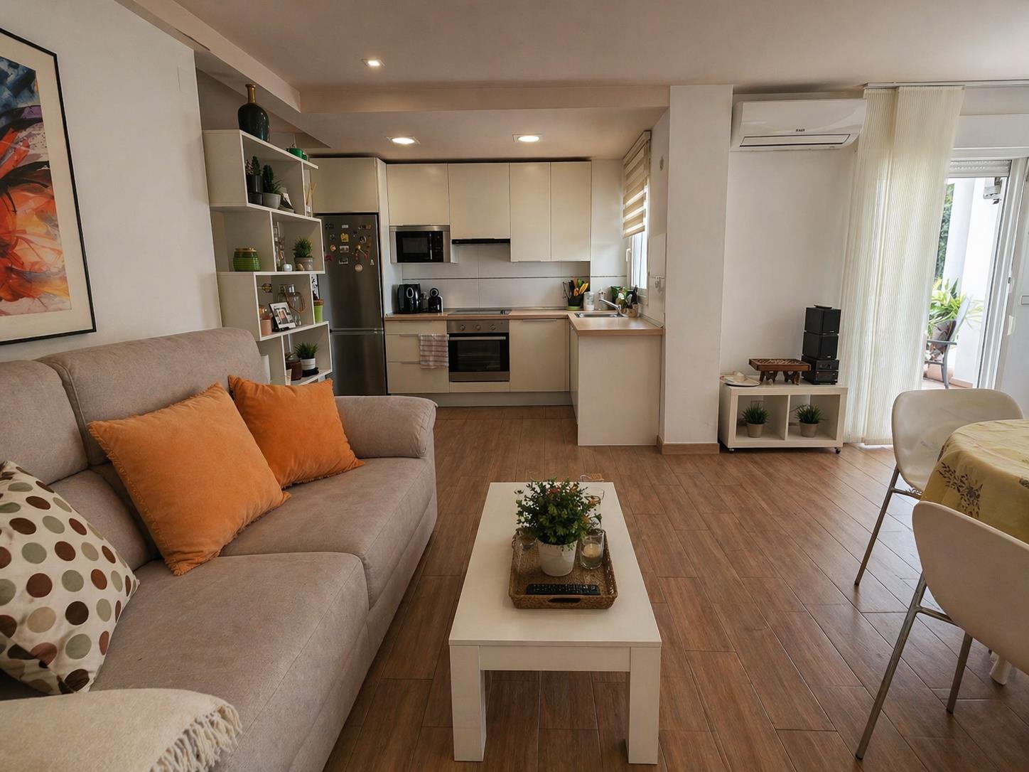Salón-comedor integrado con cocina abierta de diseño funcional, suelos de gres efecto madera, aire acondicionado y acceso directo a la terraza exterior.