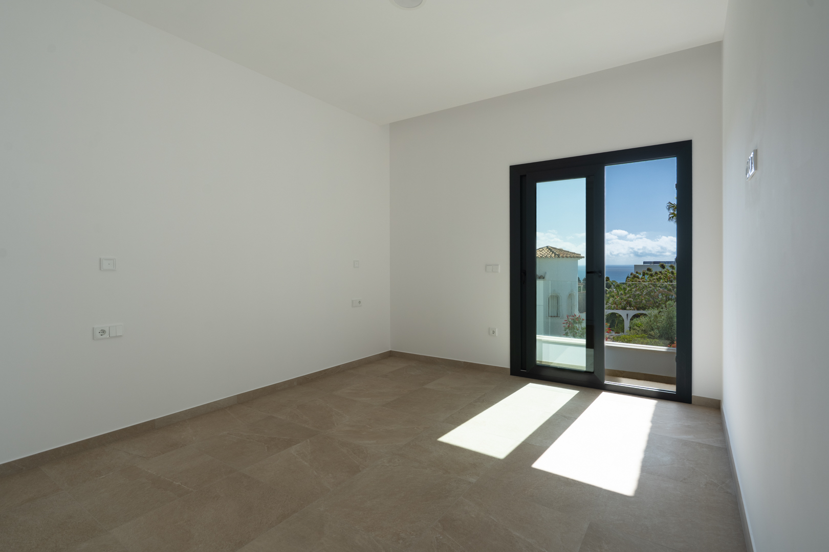 Dormitorio luminoso con suelos porcelánicos de gran formato y acceso directo a una terraza privada con vistas despejadas al mar Mediterráneo.