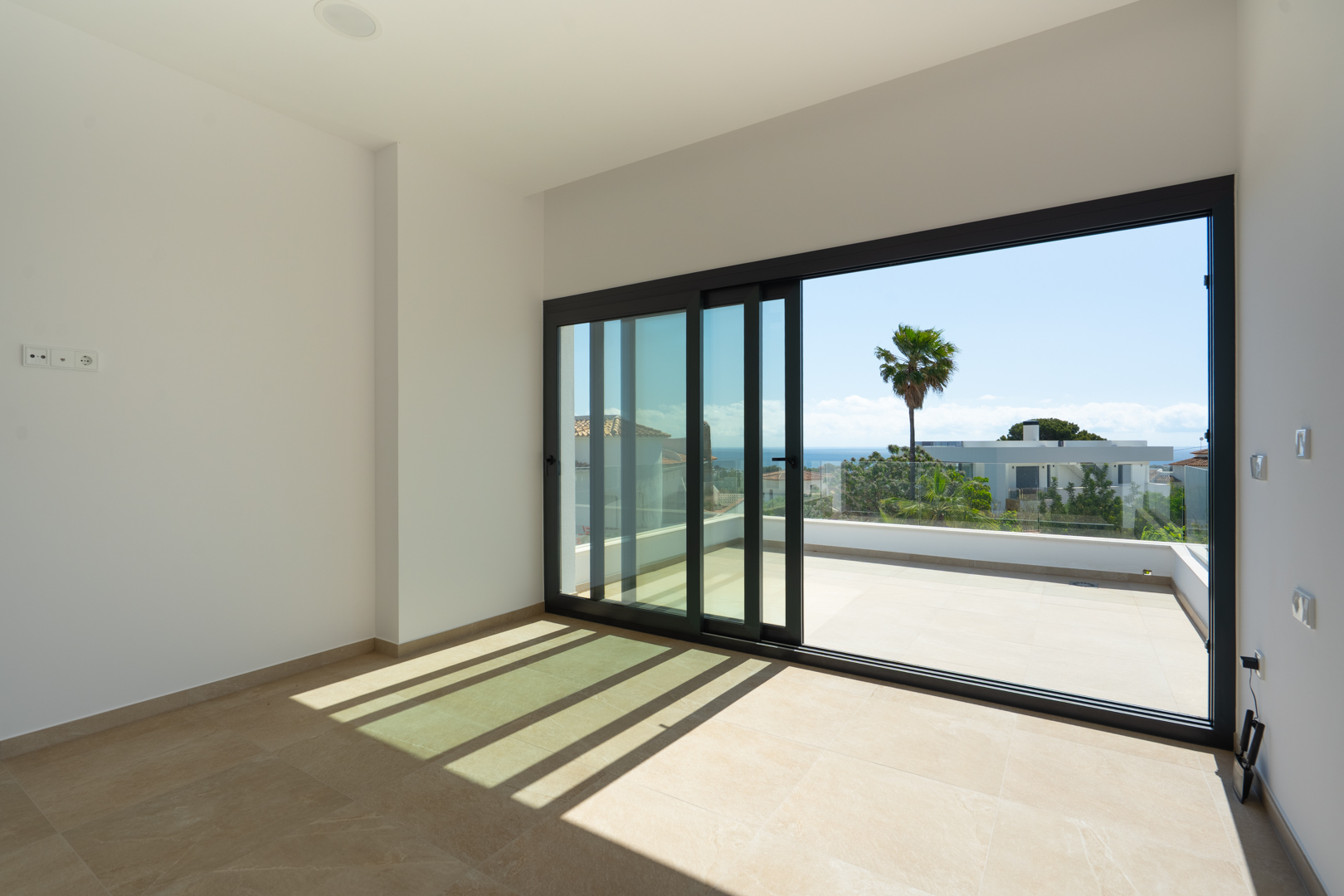 Dormitorio luminoso con suelos porcelánicos y grandes ventanales correderos que dan acceso a una terraza privada con vistas despejadas al mar Mediterráneo.