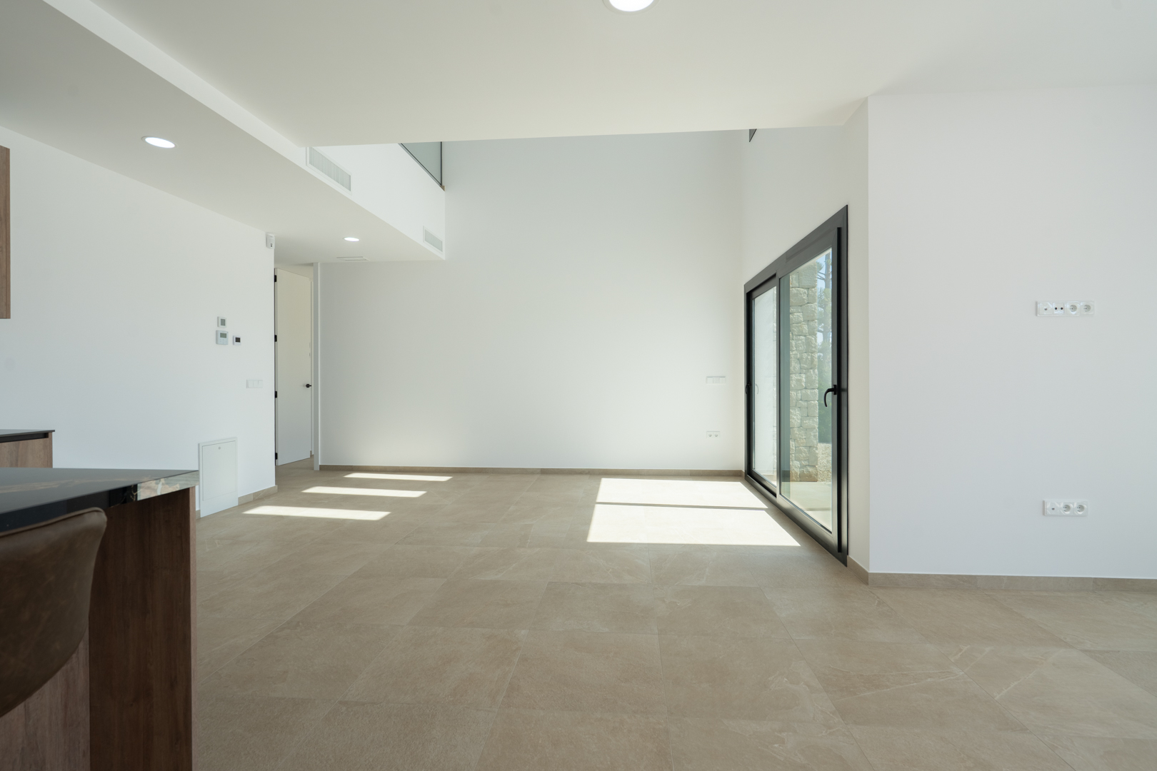 Salón-comedor de concepto abierto con techos de doble altura, suelos porcelánicos de gran formato y grandes ventanales que aportan abundante luz natural.