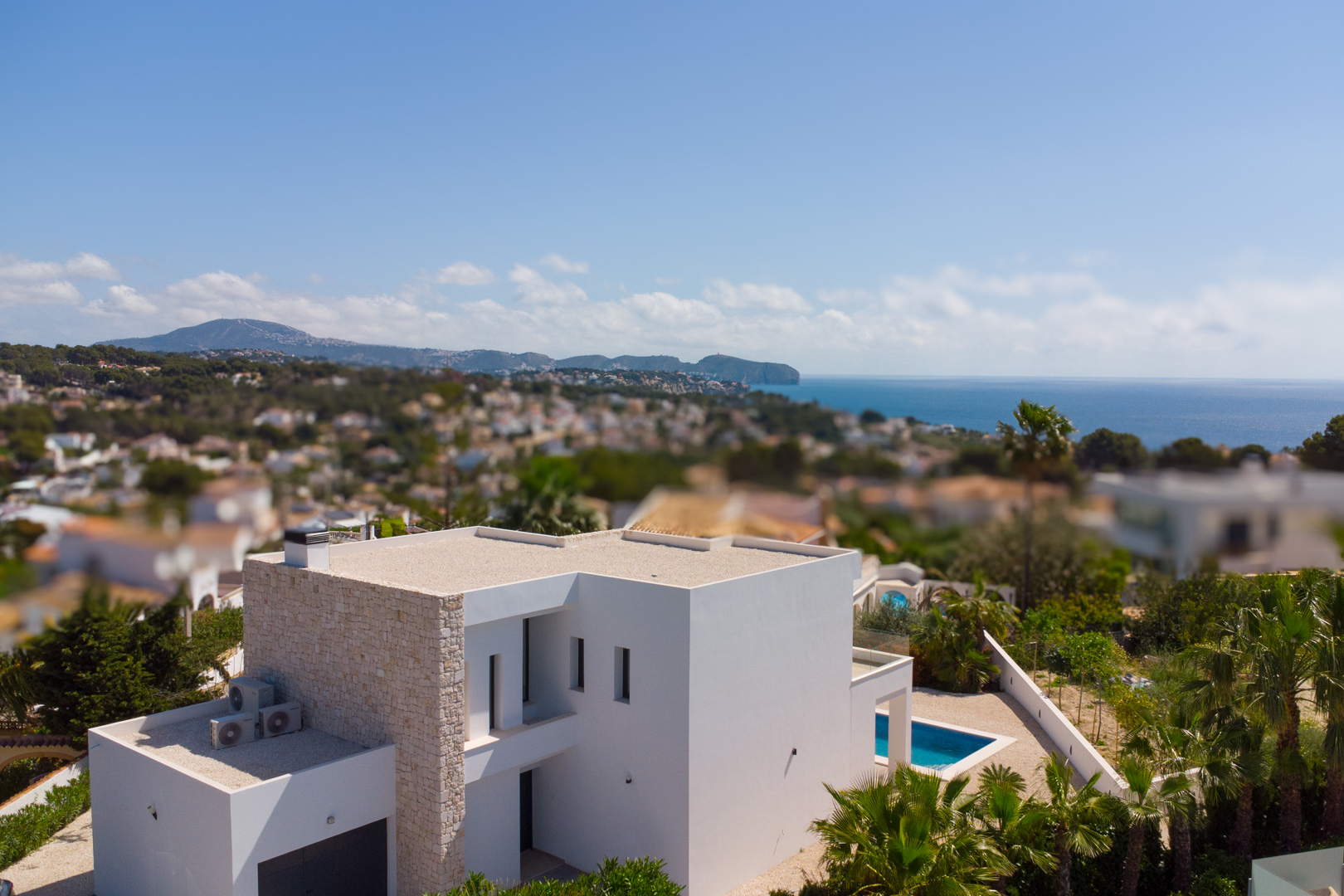 Vista aérea de la villa de arquitectura moderna con fachada blanca y detalles en piedra natural, destacando la piscina y las vistas panorámicas al mar Mediterráneo.