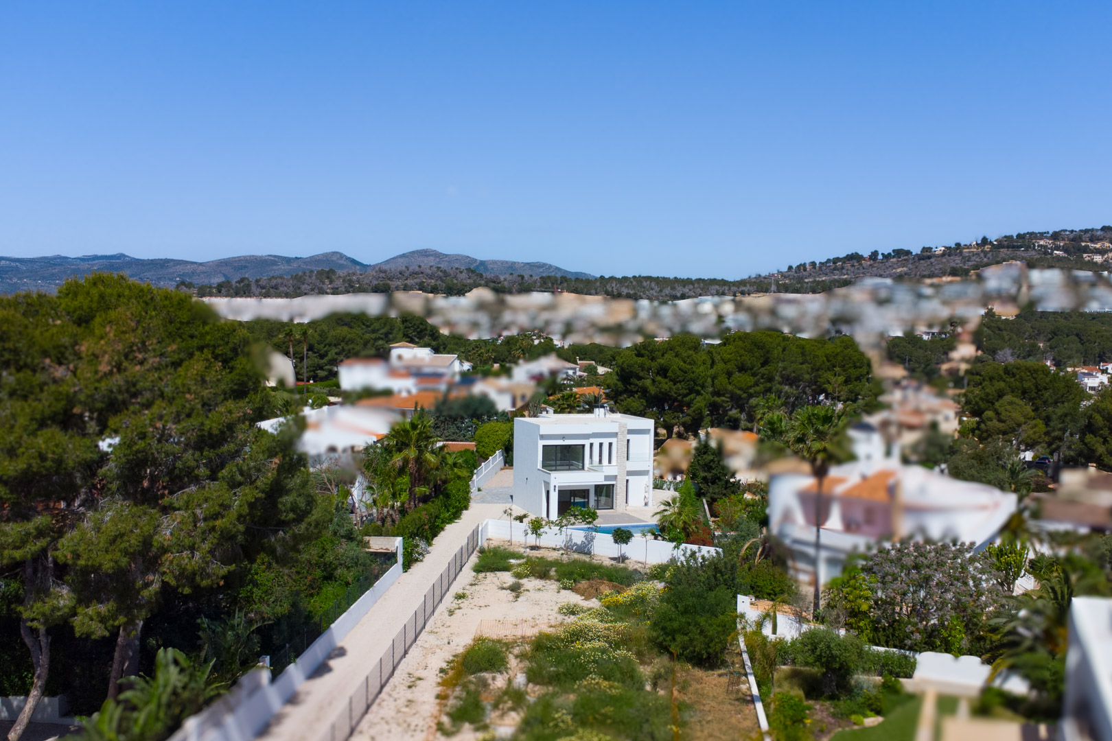 Vista aérea de la villa de arquitectura moderna situada en una amplia parcela llana, rodeada de vegetación mediterránea y con vistas a las montañas.