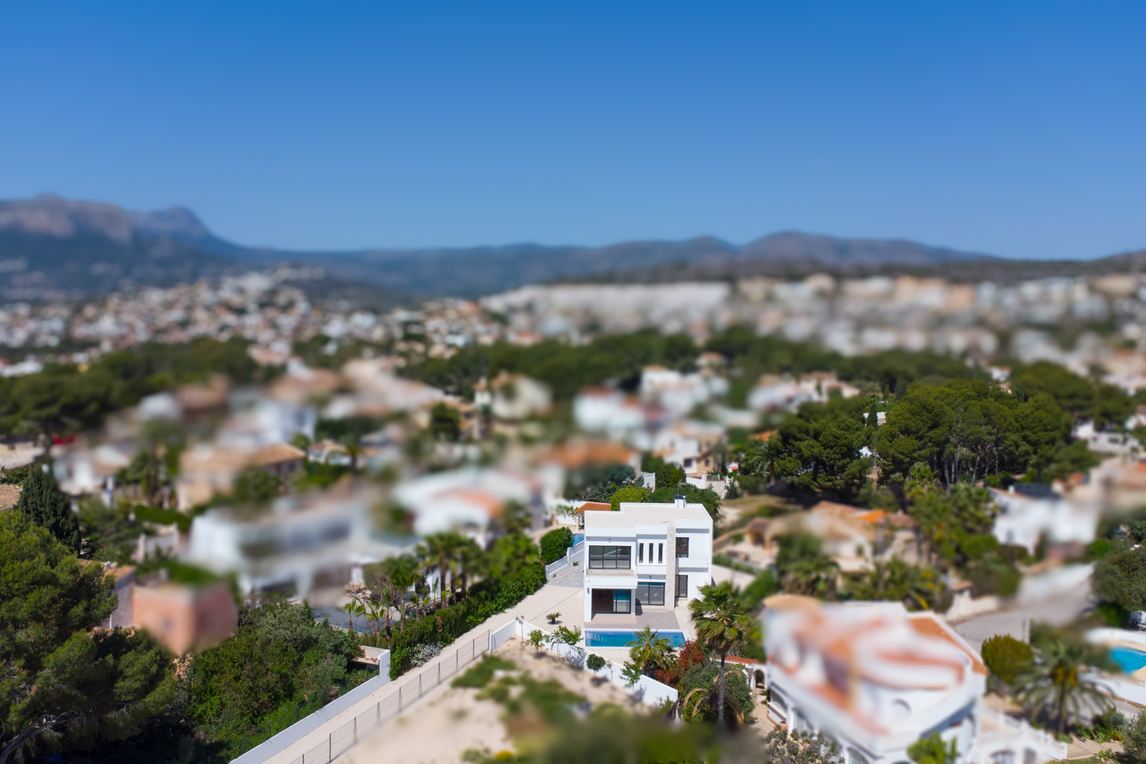 Vista aérea de la villa moderna con fachada blanca y piscina, ubicada en una amplia parcela en La Fustera con vistas panorámicas hacia la costa y las montañas.