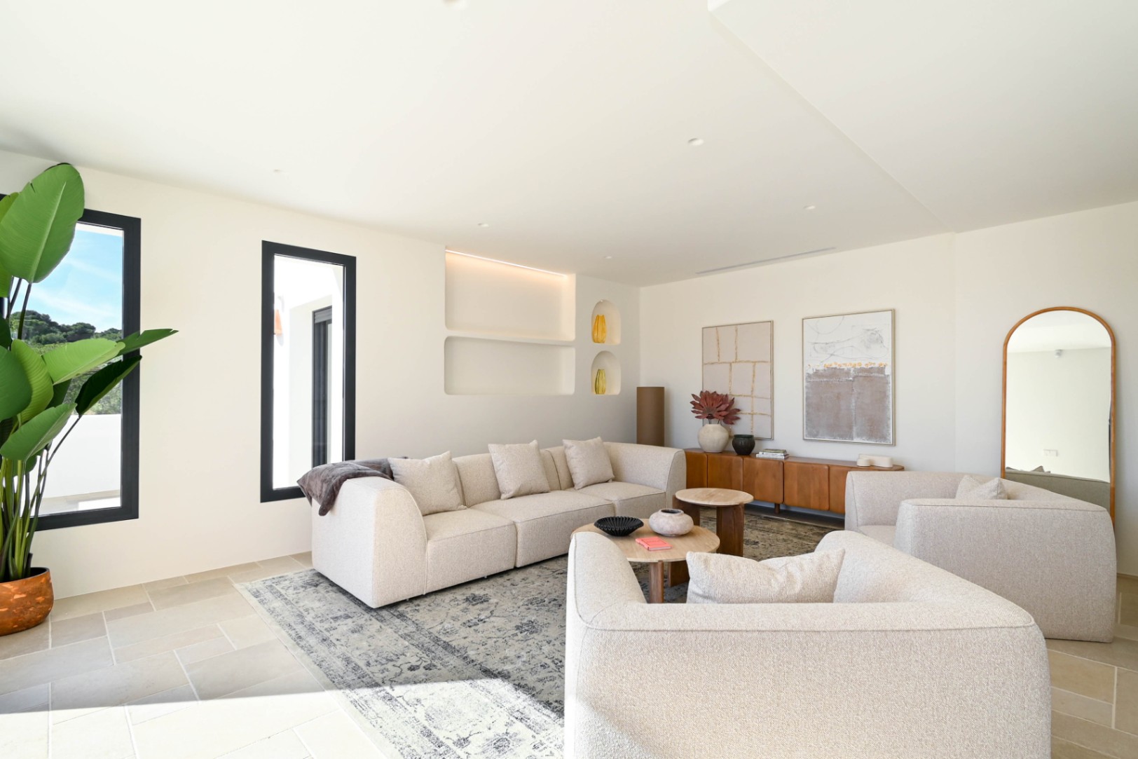 Salón luminoso con sofás de tonos neutros, hornacinas decorativas con iluminación LED integrada y suelos de piedra natural que realzan el diseño contemporáneo y espacioso.
