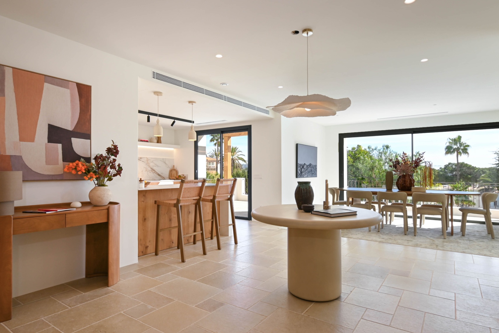 Zona de estar de concepto abierto con suelos de piedra natural, cocina integrada con isla de madera y comedor luminoso con acceso directo a la terraza mediante grandes ventanales.