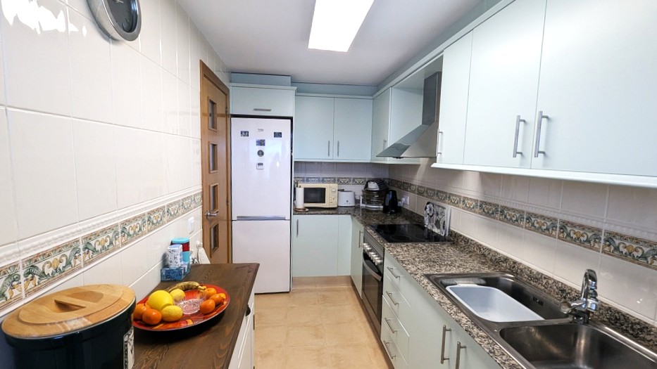 Cocina funcional tipo galera con armarios azules claros, encimeras de granito moteado y paredes alicatadas blancas con cenefa decorativa. Equipada con vitrocerámica, horno y fregadero. Cocina funcional tipo galera con armarios azules claros, encimeras de granito moteado y paredes alicatadas blancas con cenefa decorativa. Equipada con vitrocerámica, horno y fregadero.