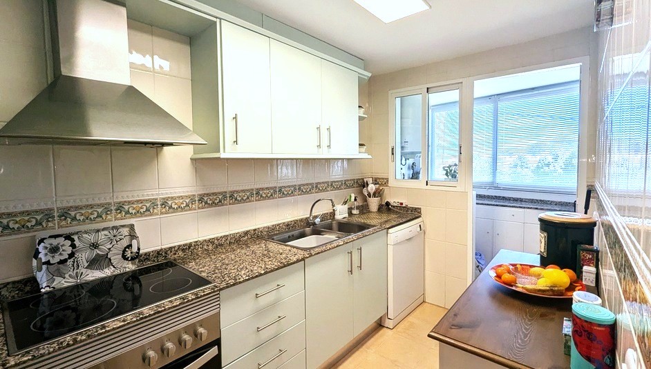 Cocina independiente equipada con encimeras de granito, campana de acero inoxidable y azulejos decorativos. Incluye acceso visual a la zona de lavadero contigua.