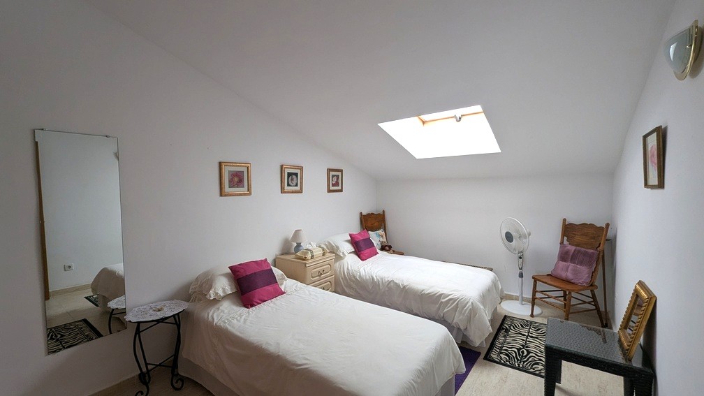 Dormitorio abuhardillado con dos camas individuales, claraboya que aporta luz natural y suelos de gres en tonos neutros.