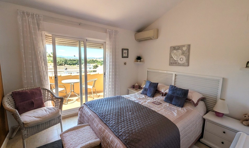 Dormitorio principal con techo inclinado, acceso directo a una terraza privada con vistas al Montgó, aire acondicionado y mobiliario en tonos blancos.