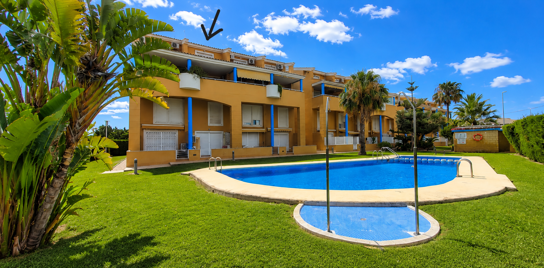 El edificio de apartamentos amarillo de la comunidad, con pilares azules, persianas blancas y balcones, da a la gran piscina comunitaria y jardines cuidados. El dúplex está en la planta superior. El edificio de apartamentos amarillo de la comunidad, con pilares azules, persianas blancas y balcones, da a la gran piscina comunitaria y jardines cuidados. El dúplex está en la planta superior.