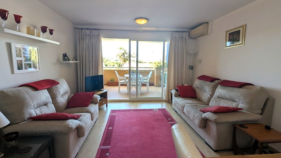 Salón luminoso con suelos de gres, sofás con detalles en rojo y acceso directo a una terraza amueblada con vistas despejadas a través de puertas correderas.