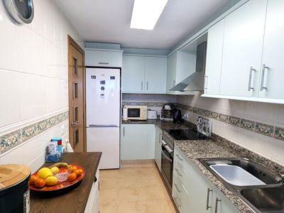 Cocina funcional tipo galera con armarios azules claros, encimeras de granito moteado y paredes alicatadas blancas con cenefa decorativa. Equipada con vitrocerámica, horno y fregadero.