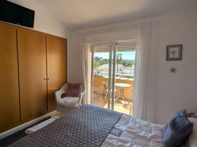 Dormitorio con armario empotrado de madera y acceso directo a un balcón privado, que ofrece vistas a tejados, palmeras y colinas lejanas desde su pequeña zona de asiento.
