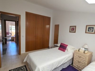 Dormitorio con dos camas individuales, armario empotrado de madera y mesita de noche. Una puerta abierta revela una terraza exterior.