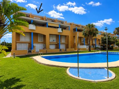 El edificio de apartamentos amarillo de la comunidad, con pilares azules, persianas blancas y balcones, da a la gran piscina comunitaria y jardines cuidados. El dúplex está en la planta superior.