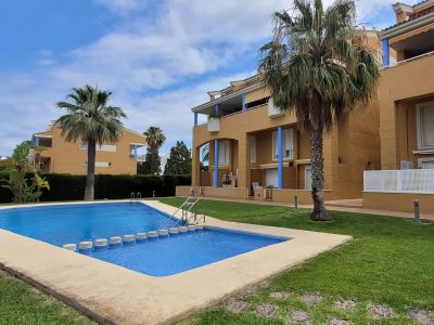La atractiva piscina comunitaria, con singulares escalones en su parte menos profunda, está rodeada de césped cuidado y edificios residenciales de tonos cálidos con acentos azules y palmeras.