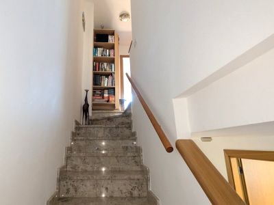 La elegante escalera interior de mármol pulido con iluminación integrada y barandilla de madera conduce al nivel superior con una estantería llena de libros.