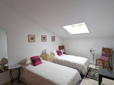 Luminoso dormitorio doble con techo abuhardillado y claraboya, ofreciendo luz natural. Dispone de dos camas individuales, mesita de noche y suelo de baldosas.
