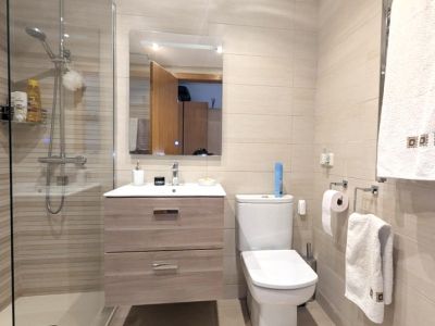 Moderno cuarto de ducha con mampara de cristal y azulejos beige rayados. Incluye mueble de lavabo flotante con dos cajones y espejo rectangular iluminado.