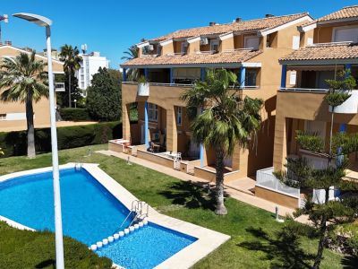 Vista elevada de la gran piscina comunitaria y el área infantil, rodeadas de césped cuidado y palmeras, con edificios residenciales al fondo.