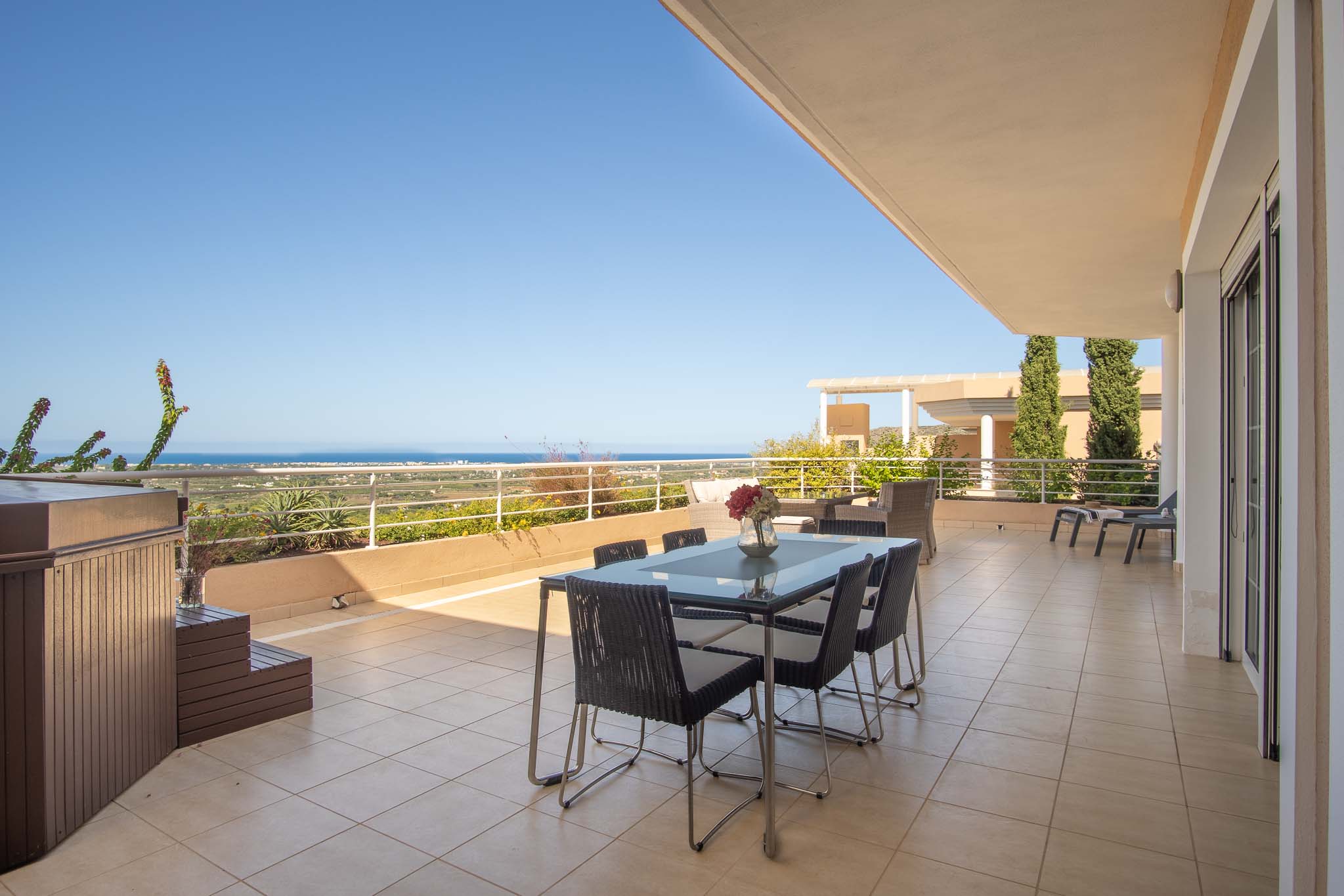 Amplia terraza con jacuzzi privado, zona de comedor exterior y vistas panorámicas al mar Mediterráneo. El suelo es de gres cerámico y cuenta con barandilla perimetral blanca.