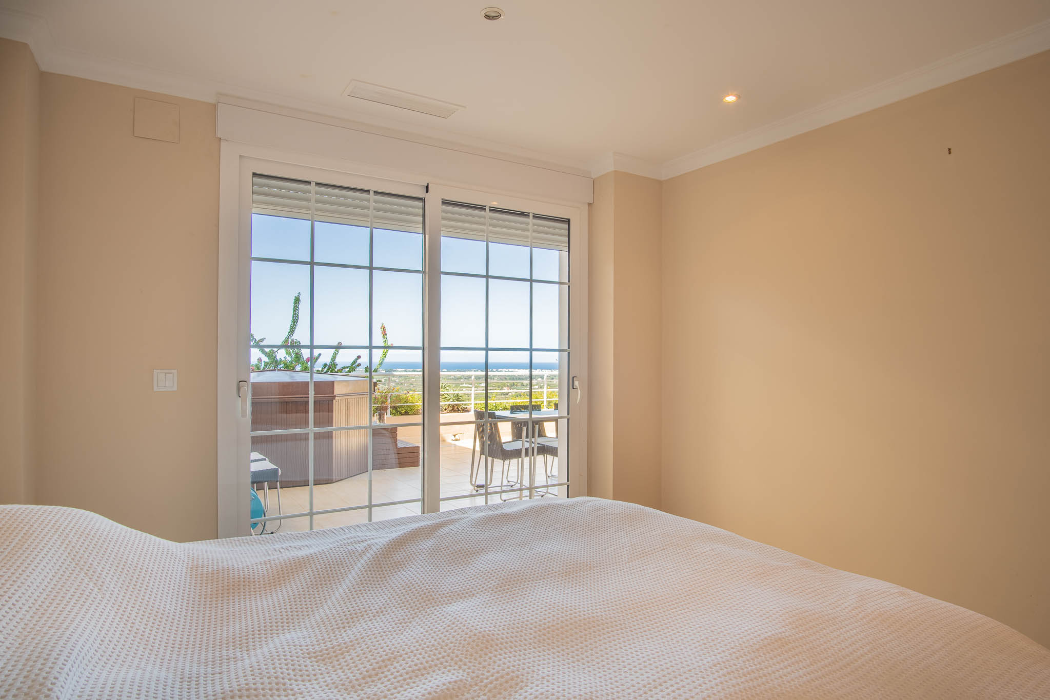 Dormitorio con acceso directo a la terraza mediante ventanales de cuadrícula. Incluye vistas al mar y al jacuzzi privado integrado en el espacio exterior.