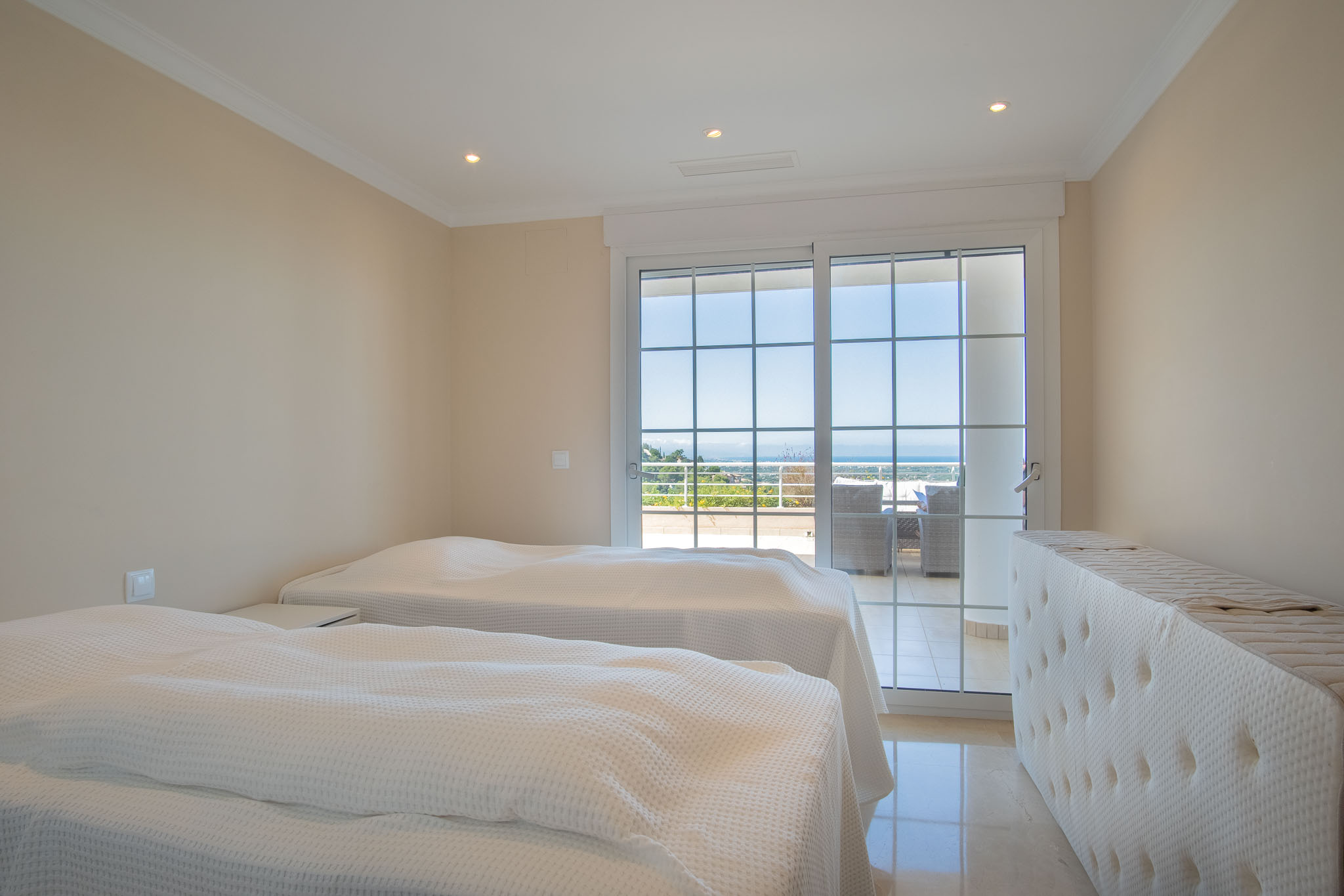 Dormitorio doble con suelos de mármol y acceso directo a la terraza mediante ventanales de cuarterones, ofreciendo vistas despejadas al mar.