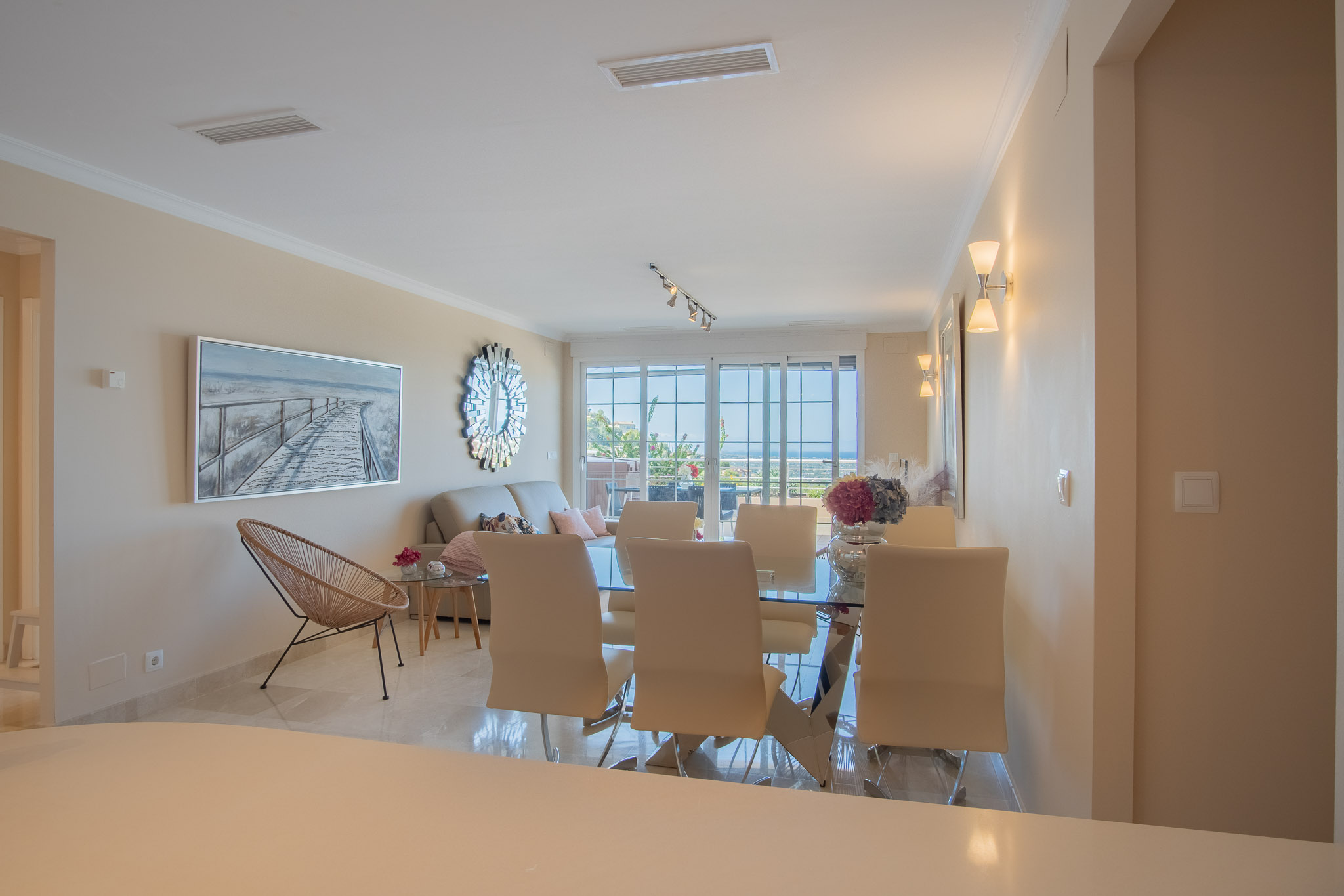 Salón-comedor de planta abierta con suelos de mármol, mesa de cristal y acceso directo a la terraza con vistas al mar a través de amplios ventanales.