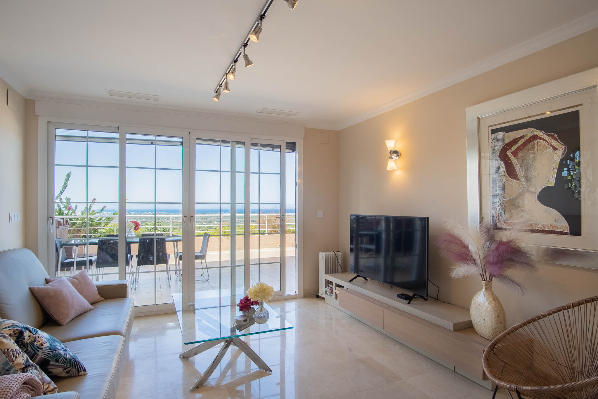 Salón luminoso con suelos de mármol, mobiliario moderno y grandes ventanales que ofrecen acceso directo a la terraza con vistas panorámicas al mar.