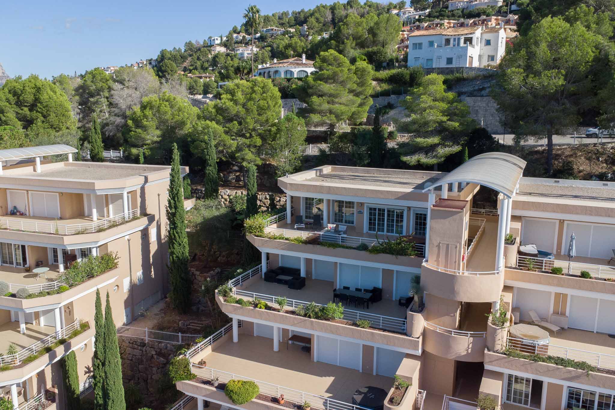 Vista exterior del complejo Las Mimosas, destacando su arquitectura escalonada con amplias terrazas privadas y fachadas en tonos tierra integradas en la ladera arbolada de La Sella.